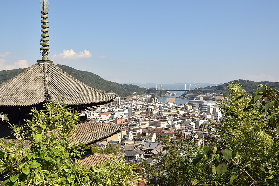 A temple pagoda roof above Onomichi rooftops with the channel and bridge beyond