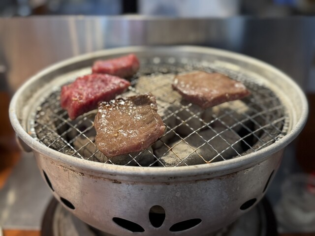 Beef cooking on a charcoal grill at Yakiniku New Hiuchi